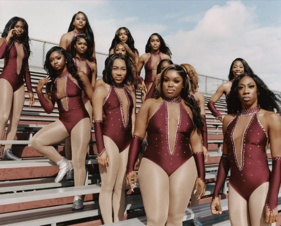 Group of Black female dancers in burgundy embellished leotards and sheer tights posing together on outdoor stadium bleachers.