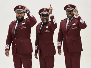 Three Black men in matching maroon peaked caps and band director uniform suits posing against a plain white studio backdrop.