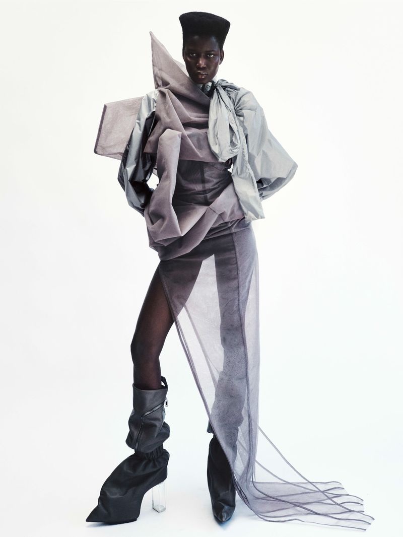 Model in avant-garde grey sculptural sheer dress and boots against a white seamless background