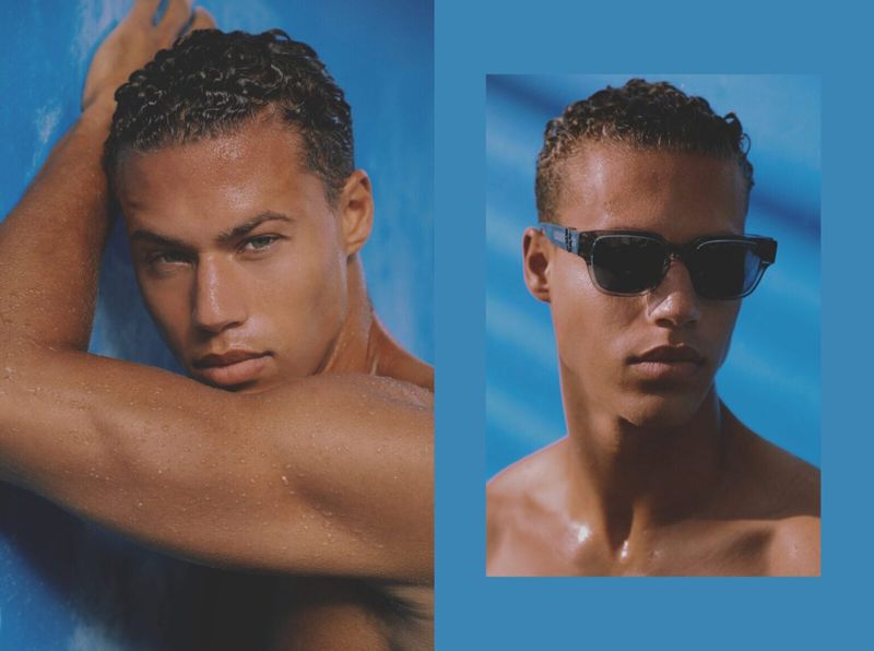 Close-up portrait of a young man with dark curly hair and sunglasses against a striking blue background