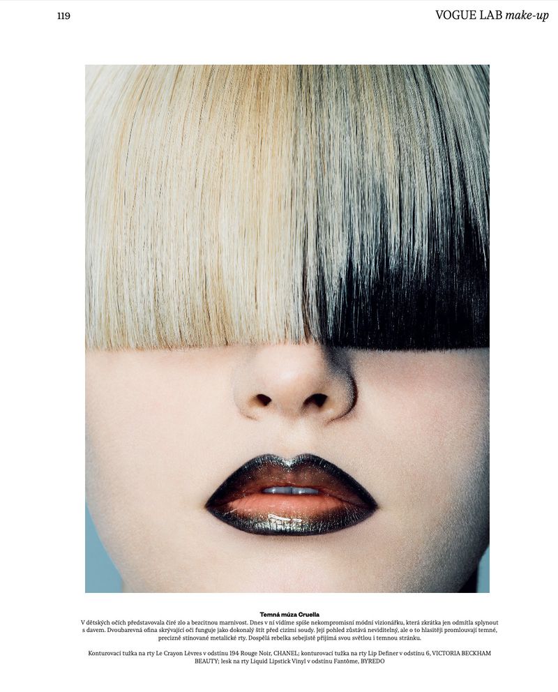 Close-up beauty portrait of a model with blunt split-tone blonde and black bangs covering her eyes and metallic ombre dark lipstick.