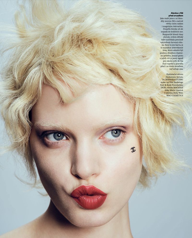 Close-up beauty portrait of model Lise Sauve with blonde textured hair, bleached brows, bold red lipstick, and a small Chanel cheek logo.