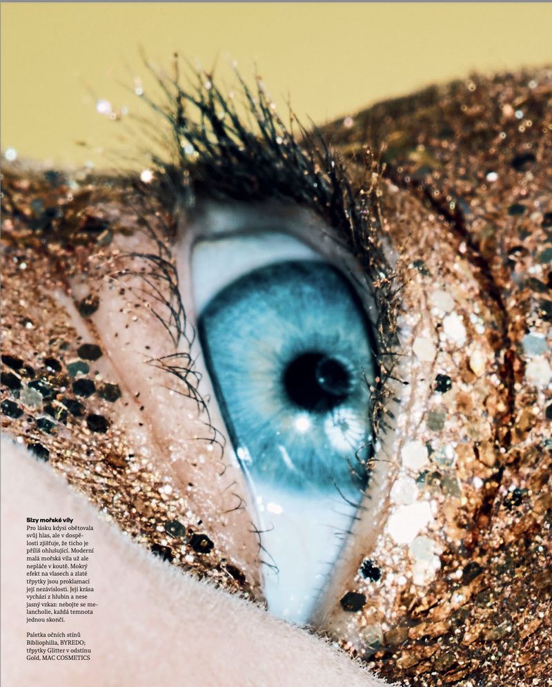 Extreme close-up of a vibrant blue eye surrounded by dense sparkling gold glitter across the eyelid and skin.