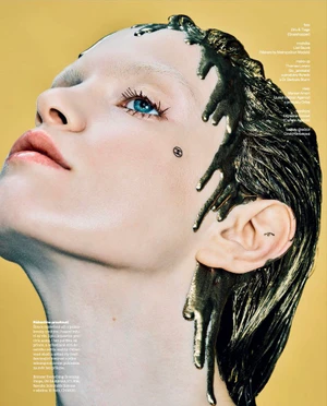 Close-up beauty portrait of model Lise Sauve with wet dripping metallic paint on her hair against a yellow background.