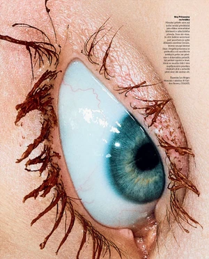 Macro beauty photograph of a blue eye with brown mascara clumped along the upper and lower eyelashes.
