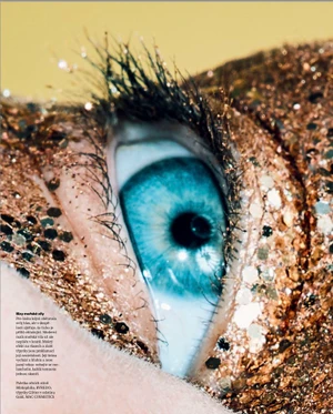 Extreme close-up of a vibrant blue eye surrounded by dense sparkling gold glitter across the eyelid and skin.