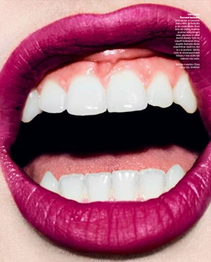 Extreme close-up of an open mouth wearing vibrant magenta lipstick with visible white teeth and tongue.