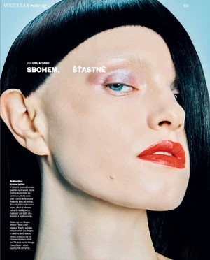 Close-up beauty portrait of a woman with graphic black micro bangs, bleached eyebrows, iridescent eyeshadow, and bright red lips.