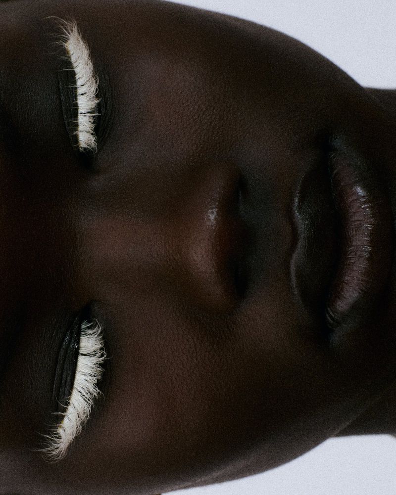 Extreme close-up beauty portrait of a Black model with closed eyes wearing textured white eyelashes.