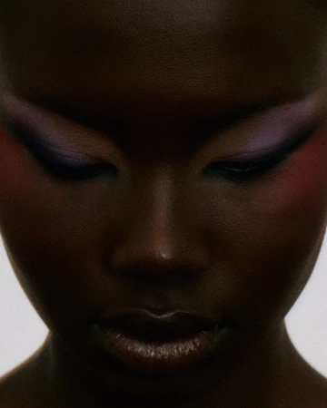 Close-up beauty portrait of a Black woman looking down, featuring dark purple eyeshadow and winged eyeliner.