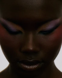 Close-up beauty portrait of a Black woman looking down, featuring dark purple eyeshadow and winged eyeliner.