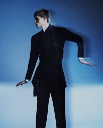 Male model in a structured black belted suit posing dynamically against a cool blue background with motion blur.