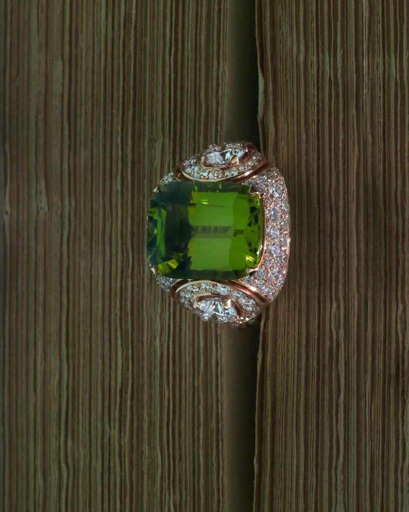 Rose gold ring featuring a faceted green peridot and diamond pavé wedged between aged book pages.