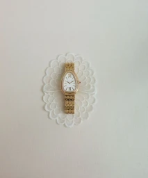 Gold Bvlgari luxury watch with a diamond bezel placed on a white ornamental lace cut-out against a clean off-white background.