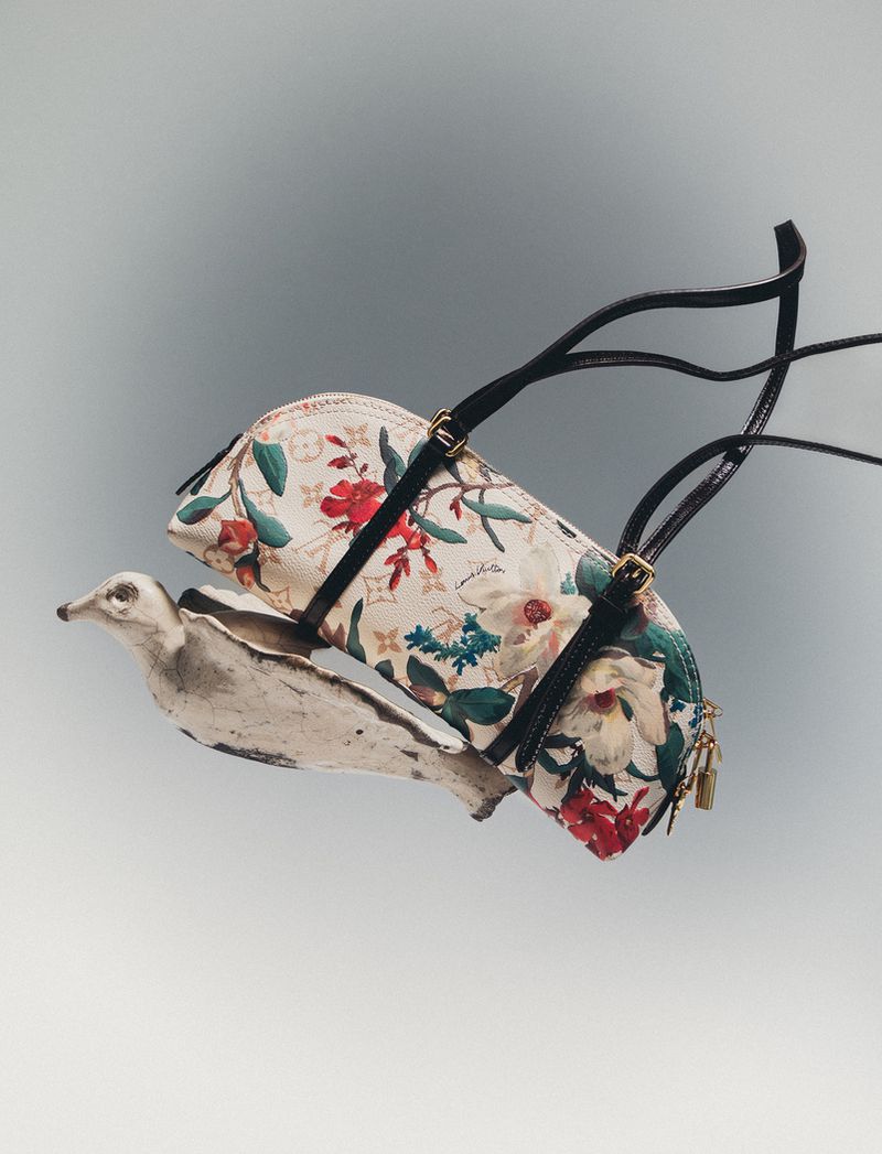 Floral print barrel handbag balanced on a sculptured bird figurine against a smooth grey gradient studio backdrop.