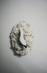 White high-heel pump with a black toe cap set against an oval sculpted floral relief on a neutral backdrop