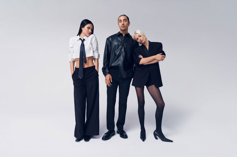 Fashion shoot of three models in a light studio wearing black and white outfits, including a crop top, leather jacket, and blazer.