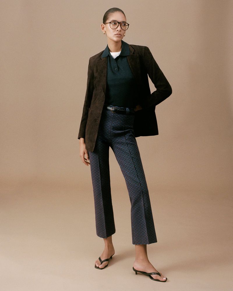 Model wearing eyeglasses, brown tailored blazer, dark green polo, patterned cropped trousers, and black kitten heel sandals.
