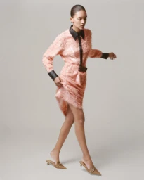 Model Summer Thompson walking in a textured pink dress with black leather trim against a light grey studio backdrop.