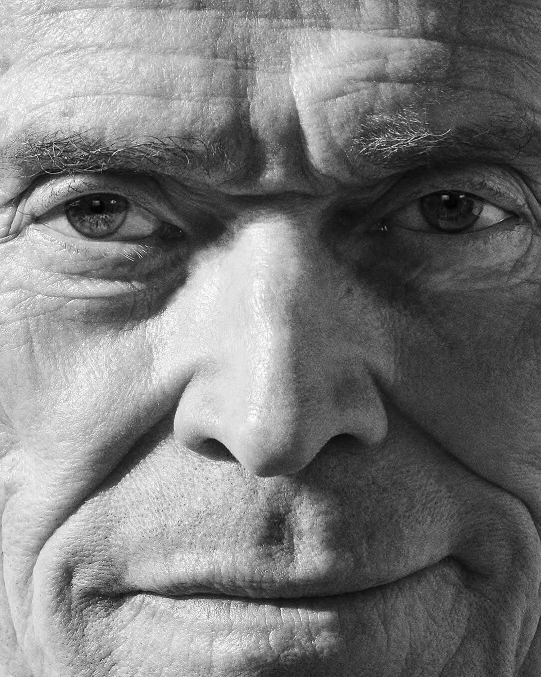 Extreme black and white close-up portrait of actor Willem Dafoe showing detailed facial expression and textured skin.