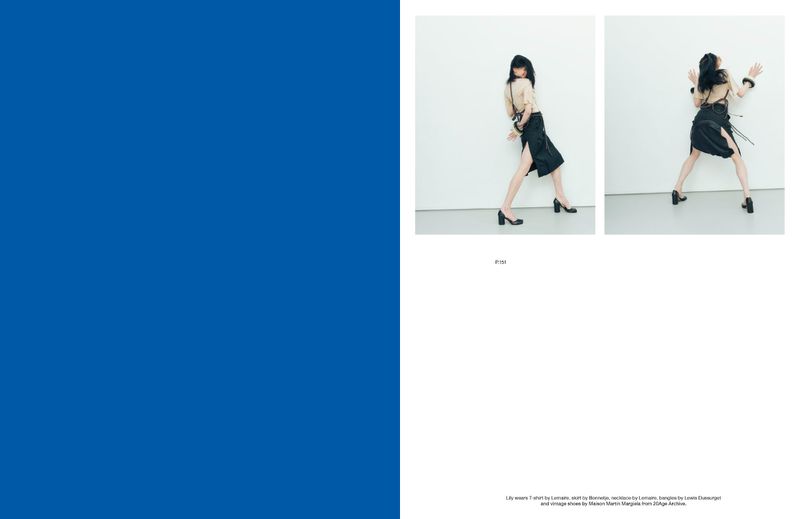 A fashion editorial shot showcases a woman in a beige shirt and black skirt, posing in front of a white wall, in a studio setting.