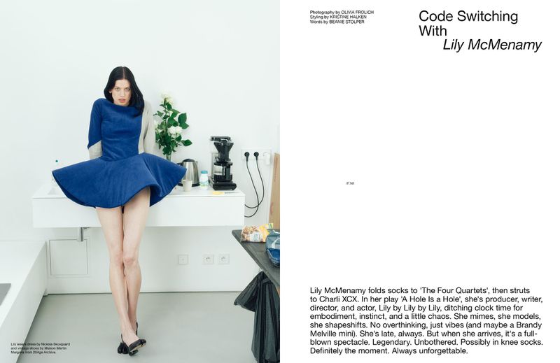 Fashion editorial shot of Lily McMenamy in a blue dress posing against a white background with minimal props and stark lighting.