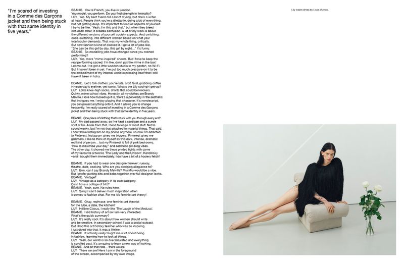 A model lounges on a cream-colored chaise lounge in a minimalist studio, showcasing a dark, fringed fashion garment and white roses.