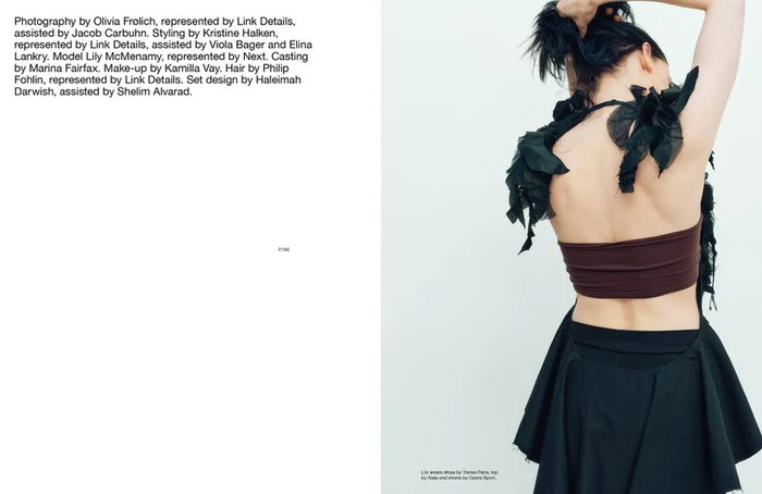 Model Lily McMenamy seen from behind wearing a brown top and black skirt against a white studio background.