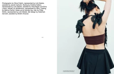 Model Lily McMenamy seen from behind wearing a brown top and black skirt against a white studio background.