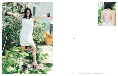 Model Lily McMenamy posing outdoors in a white dress with arms outstretched in a garden setting.