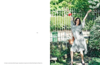Model Lily McMenamy posing with arms raised in a pleated grey dress in front of a garden fence for Endless Magazine.