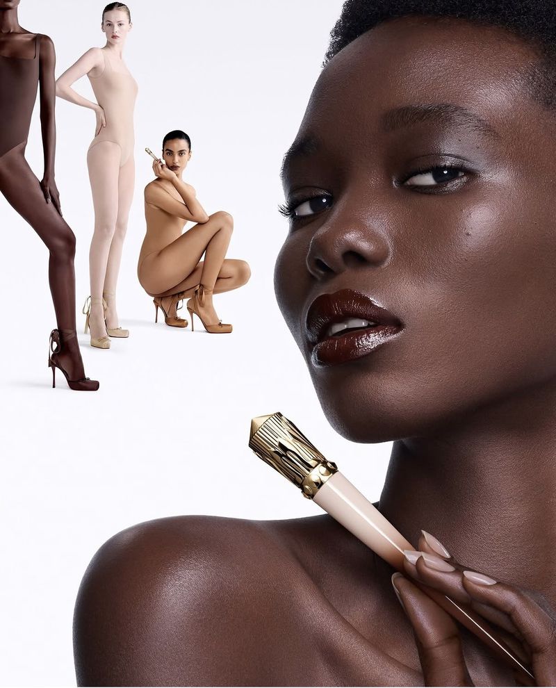 Close-up of a Black woman holding a gold-capped Louboutin lipstick wand alongside background models against a white backdrop.