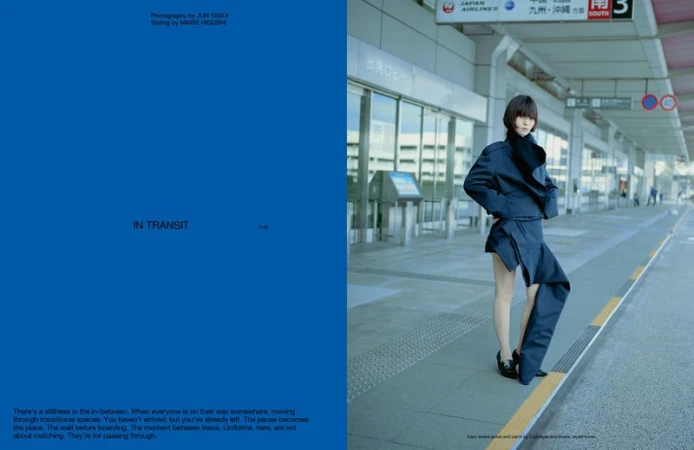 Fashion editorial shot of a woman in a navy blue deconstructed suit at an airport terminal on a cloudy day, standing next to a bus stop.