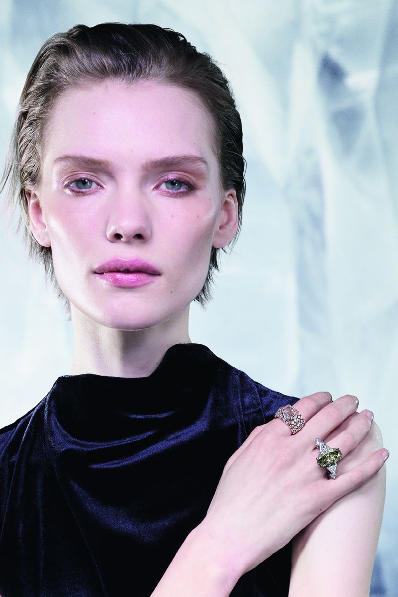 Model wearing luxury gemstone rings and a dark navy velvet garment against an icy pale blue textured background.