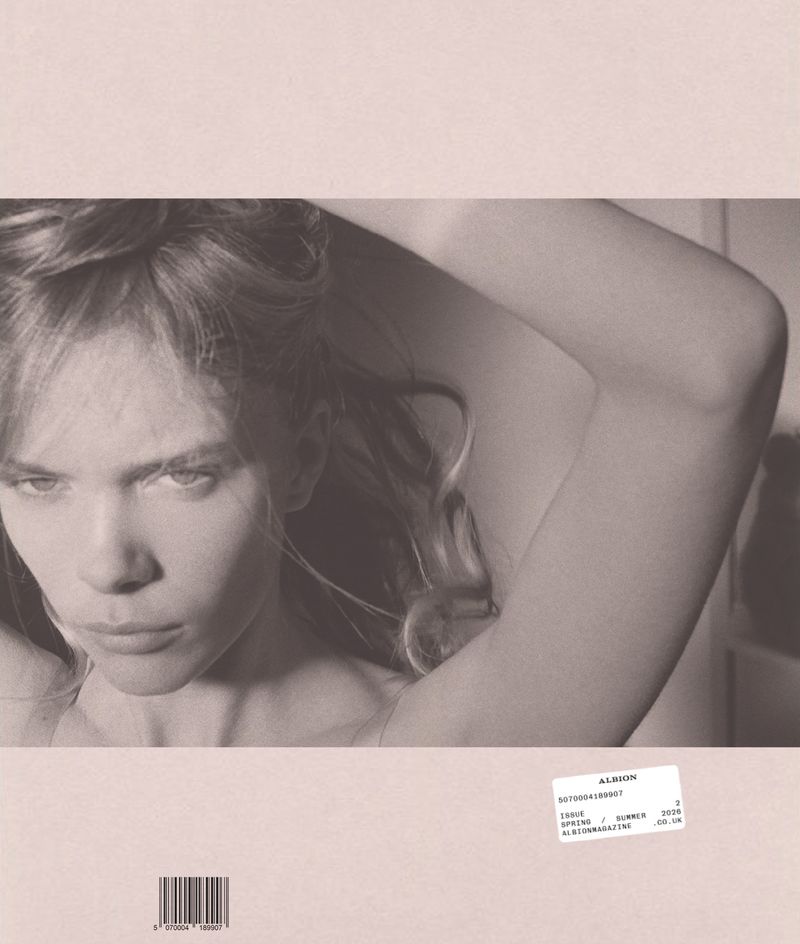 Monochrome close-up portrait of a woman with an arm raised over her head, set within a pale pink magazine cover layout.