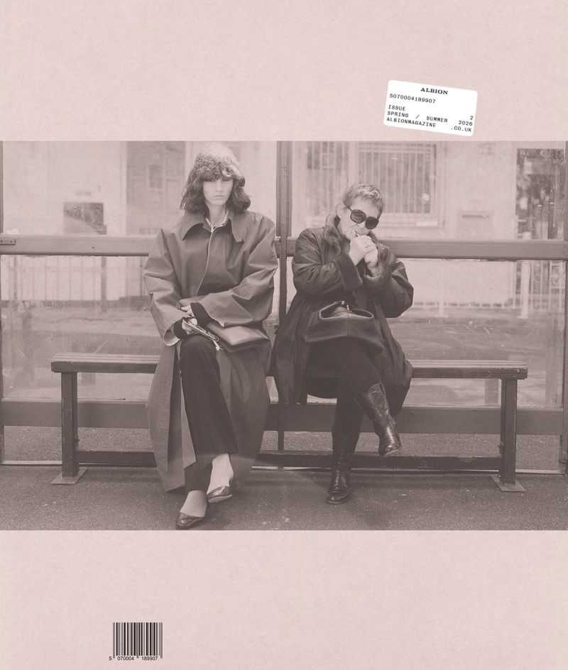 Two women wearing dark coats seated together on a bus stop bench for Albion Magazine Issue 2 cover.