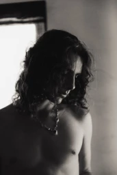 Portrait of young man with long curly hair wearing a pendant necklace for Numero Netherlands editorial by Sam Spence