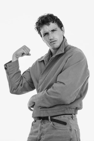 Black and white studio portrait of model Sergio Modrego posing with a flexed arm in a jacket and jeans against a white background.