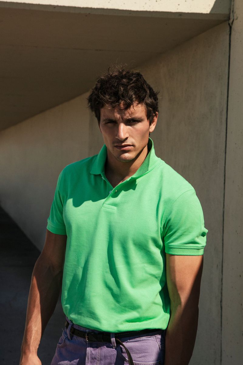 Man wearing a vibrant green polo shirt standing under a concrete architectural overhang.