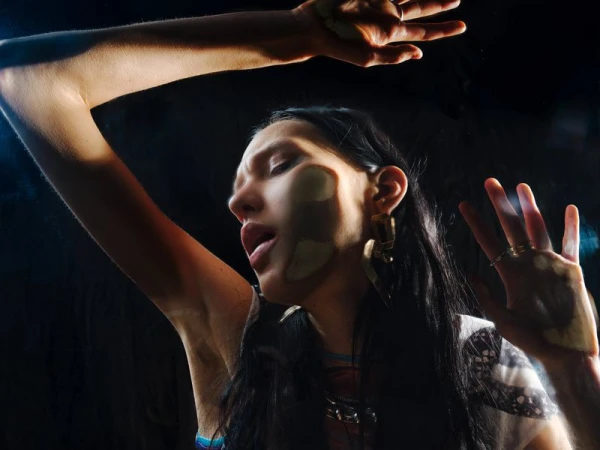 Woman pressing her face and open hands against a clear glass pane in dramatic low-key lighting against a dark background.