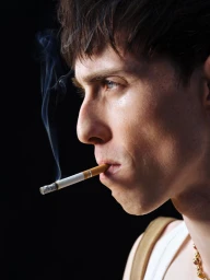 Profile close-up of a man with short brown hair smoking a lit cigarette against a solid black background.