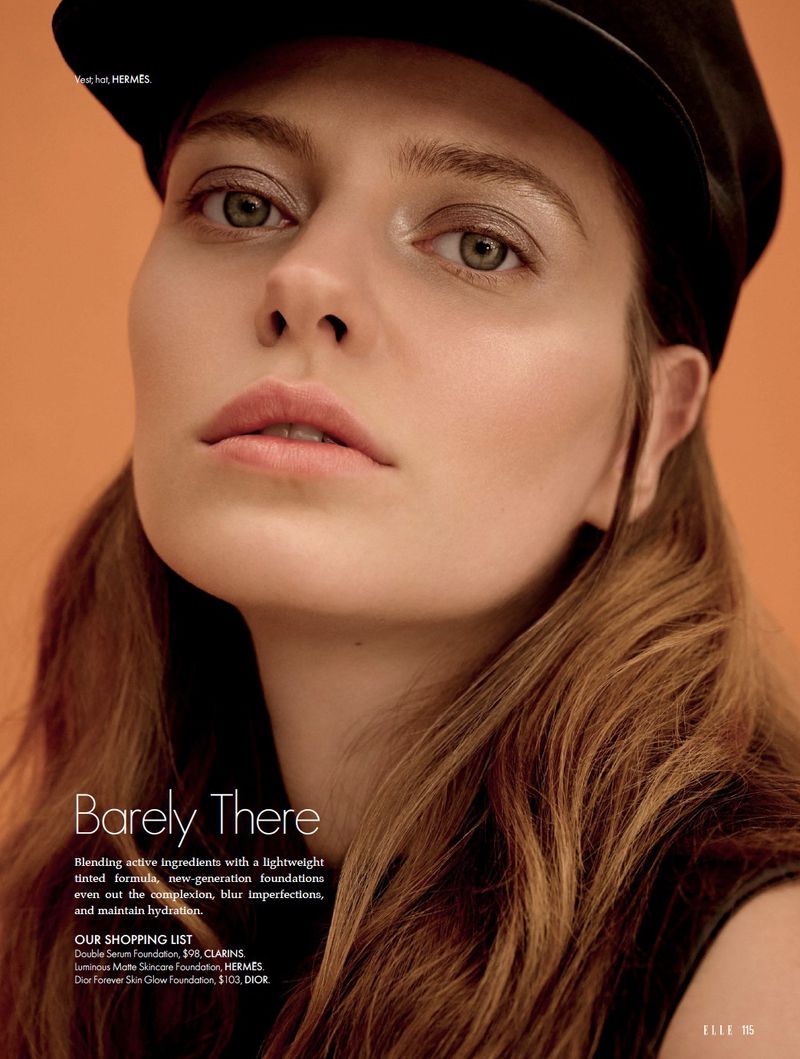 Close-up beauty portrait of model Tali Bulycheva wearing a black cap with luminous makeup against an orange backdrop.