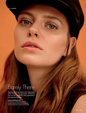 Close-up beauty portrait of model Tali Bulycheva wearing a black cap with luminous makeup against an orange backdrop.