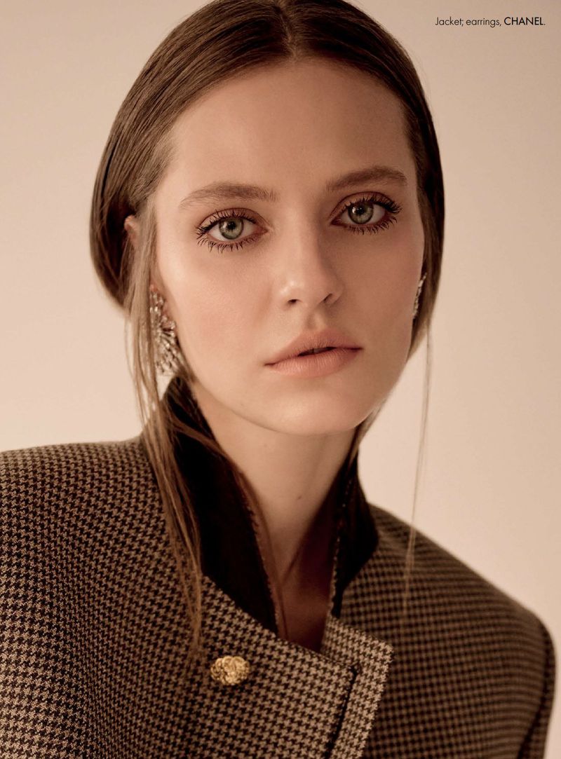 Close-up portrait of model Tali Bulycheva wearing a brown houndstooth jacket and ornate earrings against a cream backdrop.