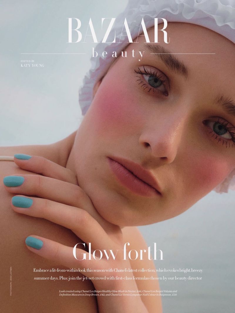Close-up beauty portrait of a woman wearing a ruffled white swim cap with vibrant pink blush and bright blue nail polish.