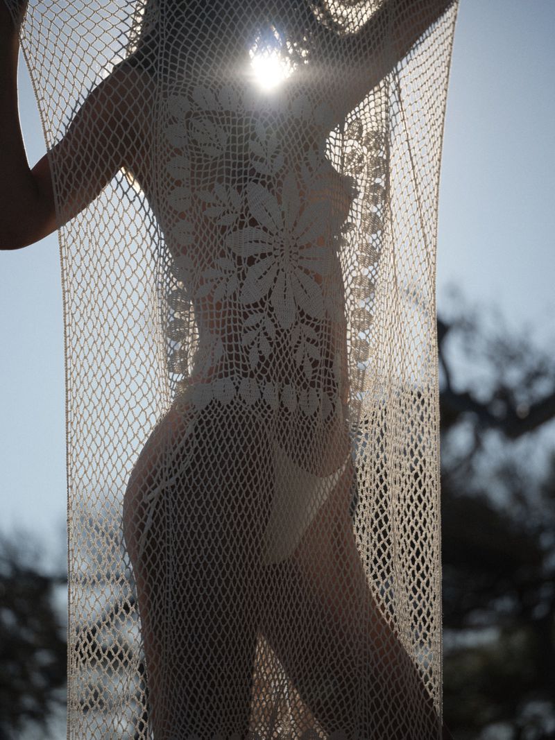 Model Lea Seelenmeyer holds a sheer floral crochet cover-up backlit by sunlight for the Magda Butrym Summer 2026 campaign.