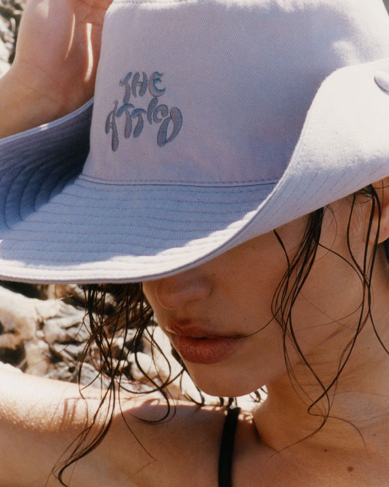 Close up of a model wearing a light blue The Attico sun hat with wet hair against rocky background