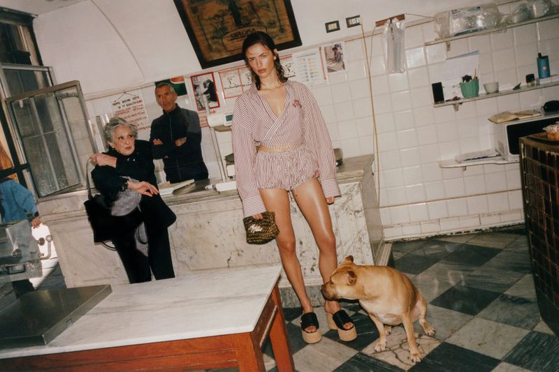 Model standing in striped shirt and shorts holding a handbag inside a traditional Italian shop