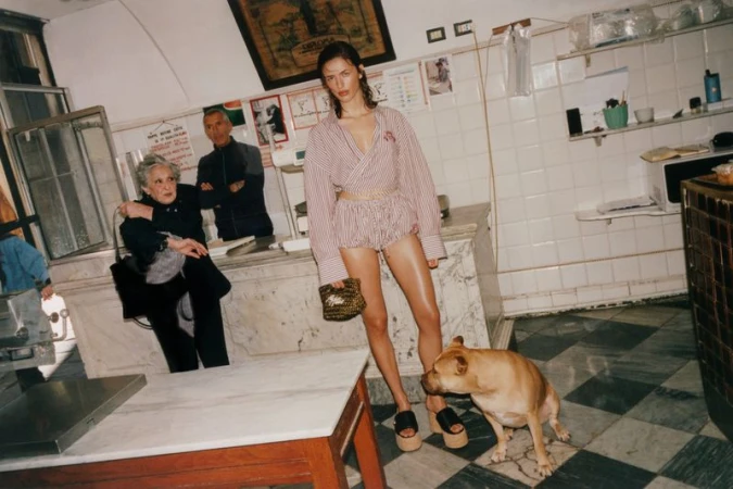 Model standing in striped shirt and shorts holding a handbag inside a traditional Italian shop