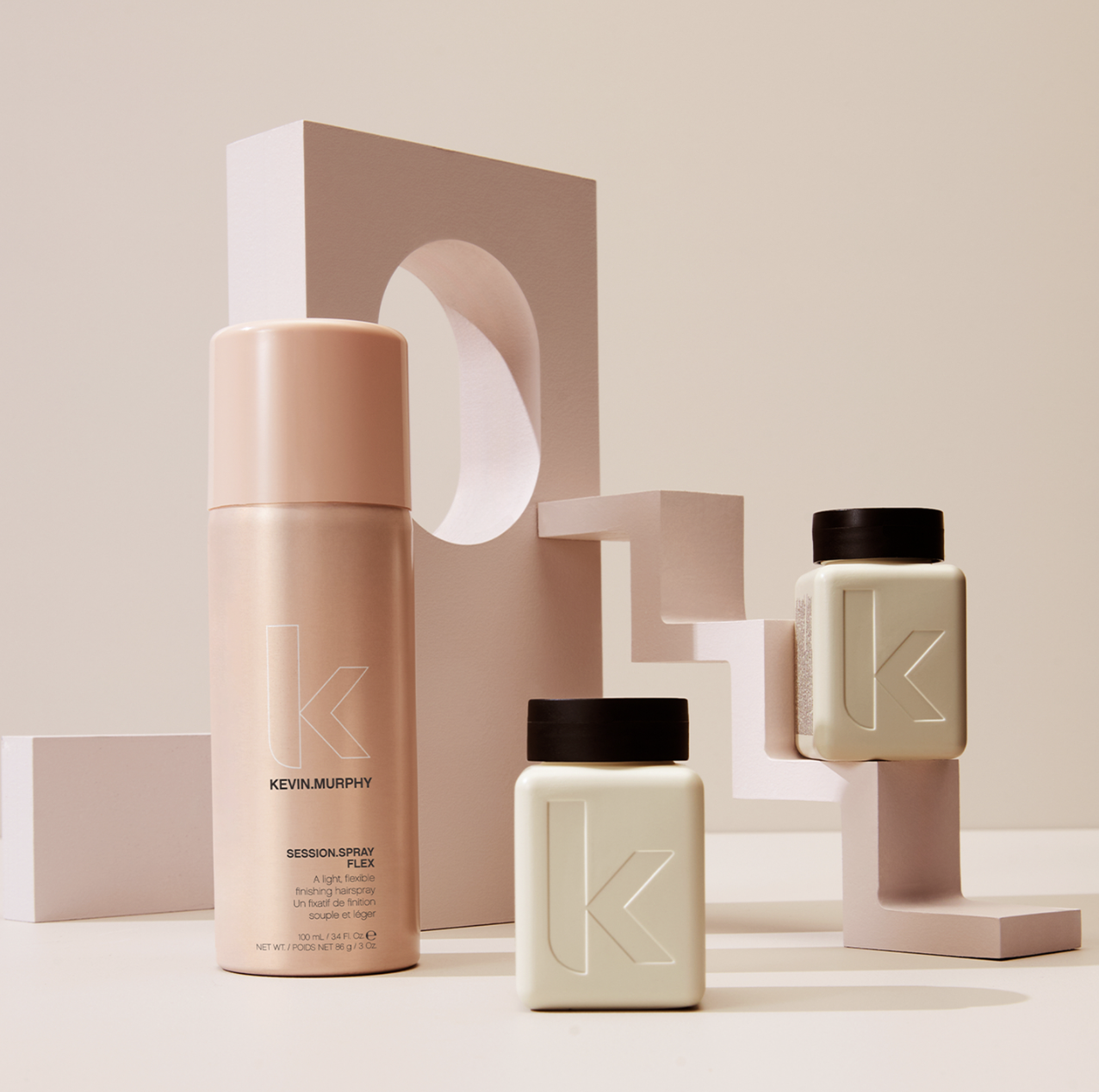 Kevin Murphy hair products are displayed on a light beige surface with stacked geometric props in matching colors in a studio setting.